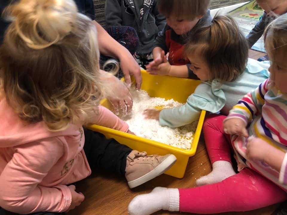 Children playing with white material in a yellow bin
