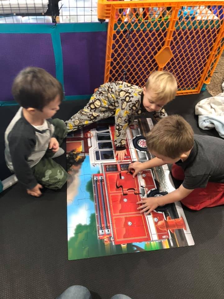 Three children playing with a fire truck floor puzzle