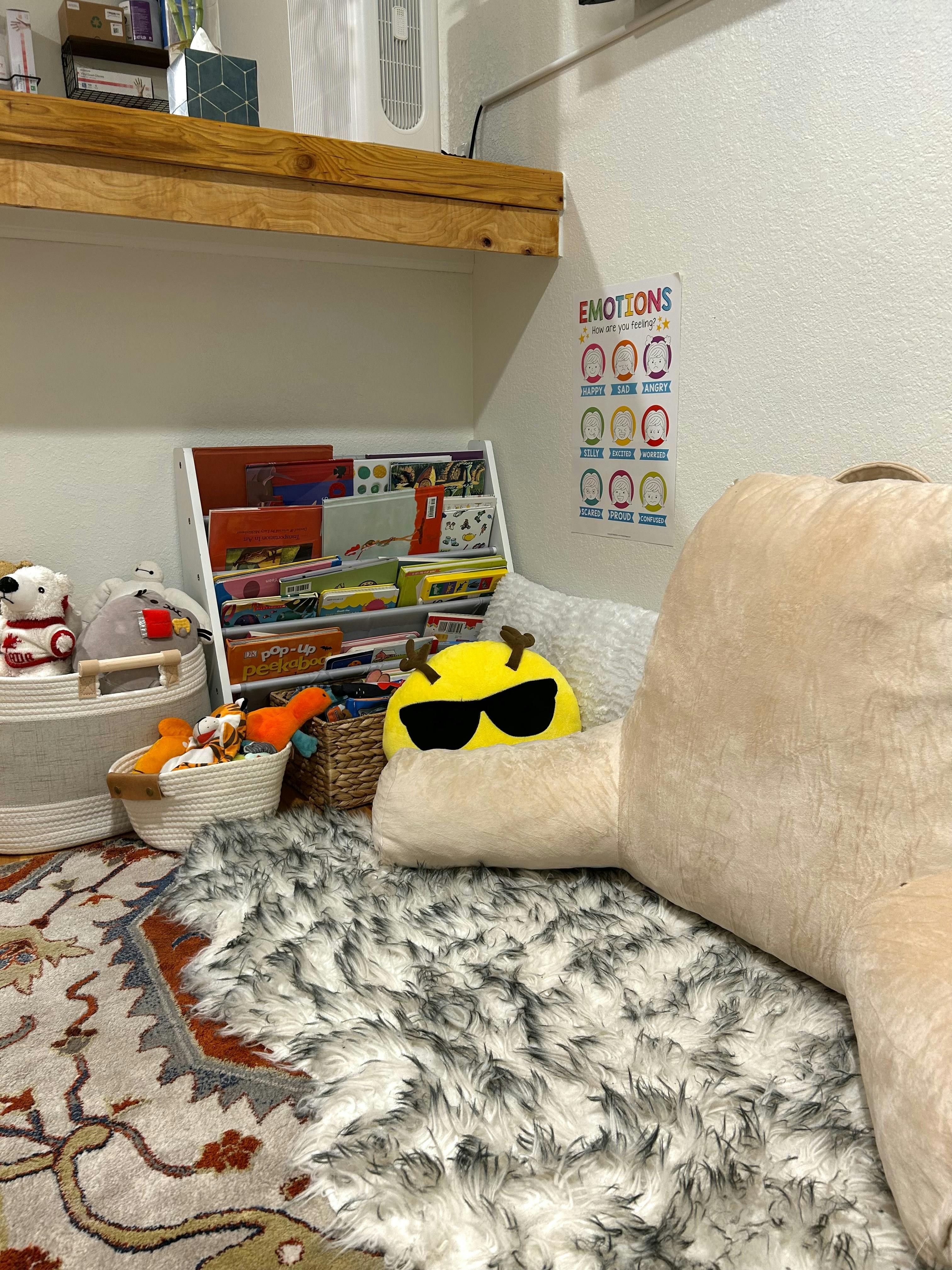 Childs reading corner with a bookshelf, floor pillows, and emotions chart