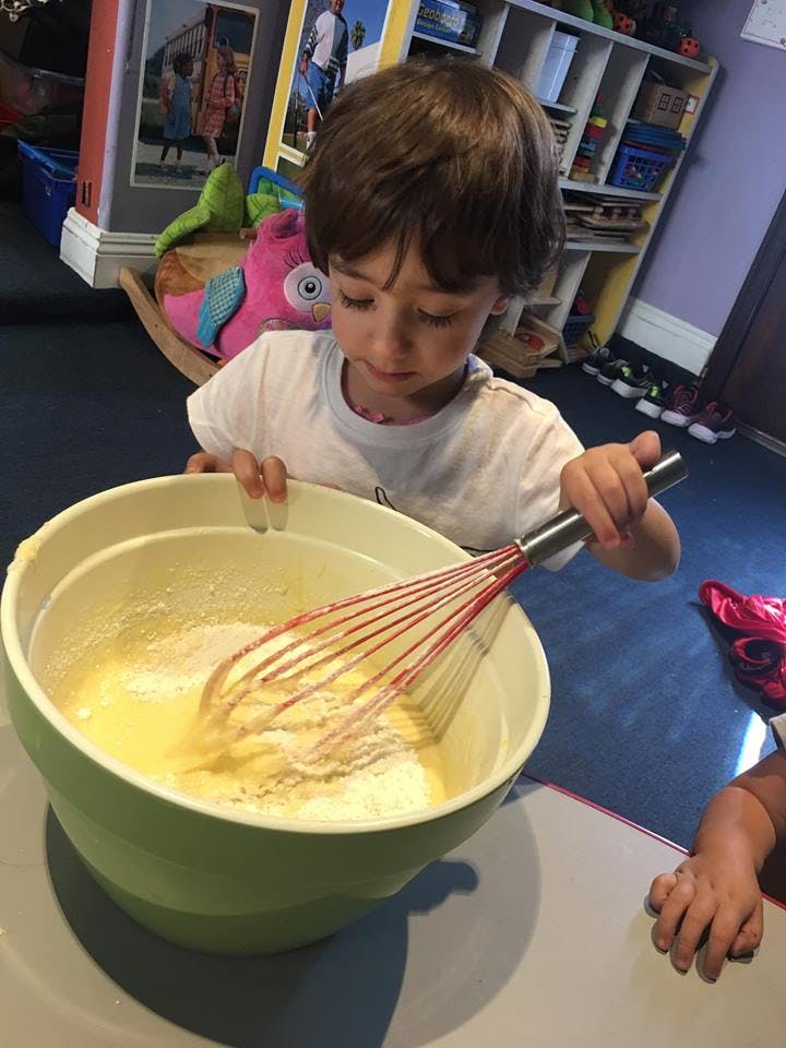 Child mixing ingredients in a bowl with a whisk