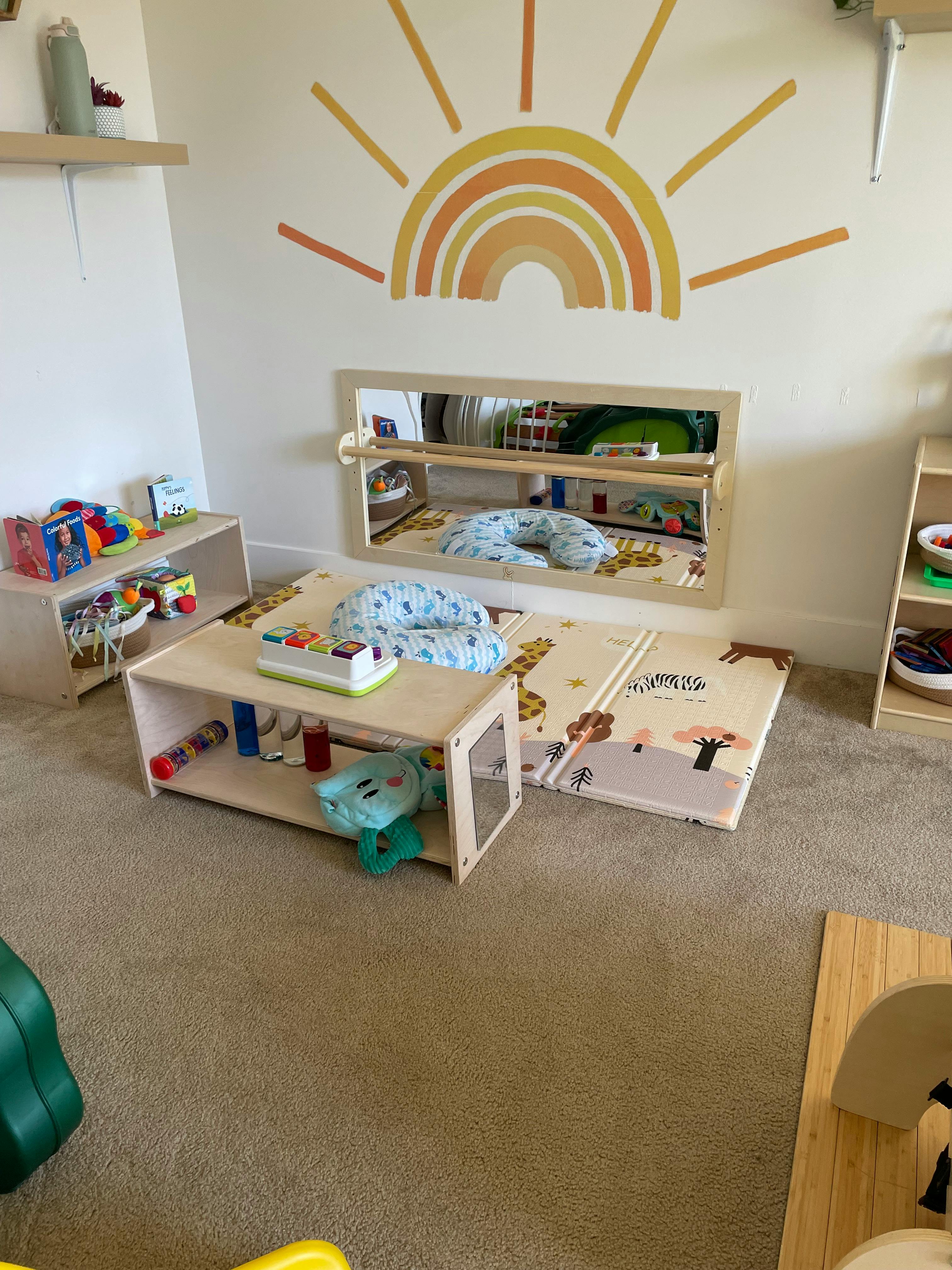 A child's play area with a sun and rainbow mural, mirror, and play mats