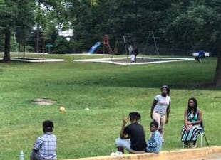 People sitting on a curb watching children play in a park