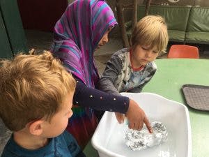 Person and two children looking at an object in a basin of water