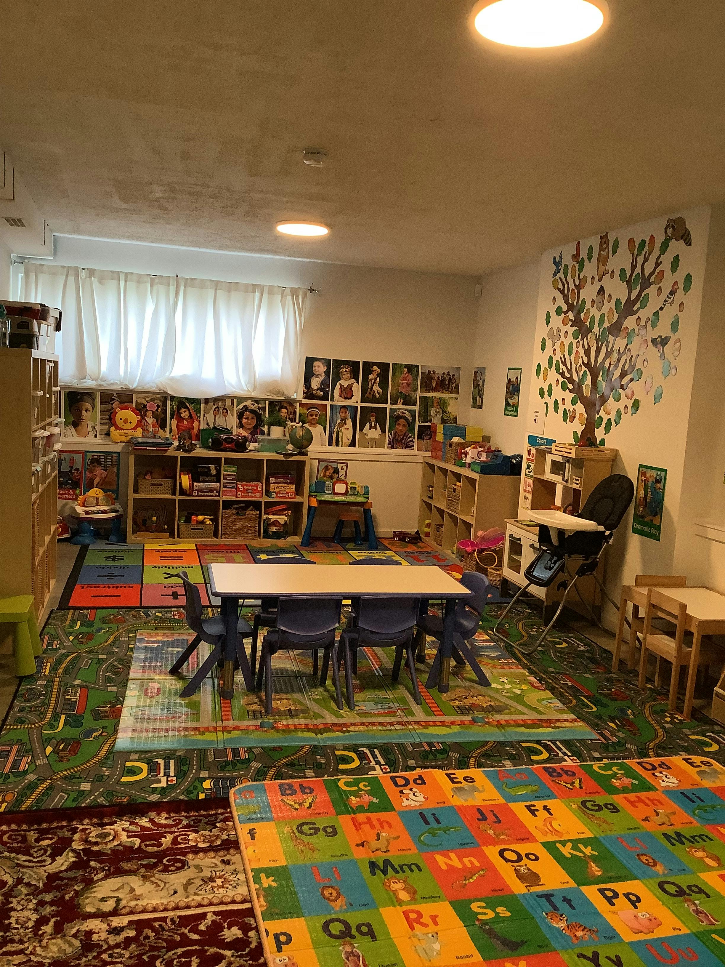 Classroom with small tables and chairs, colorful rugs, and shelves with items