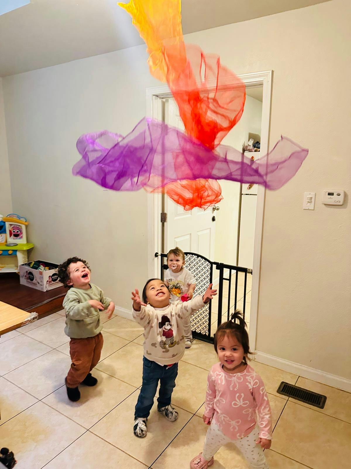 Several children looking up at colorful scarves floating in the air