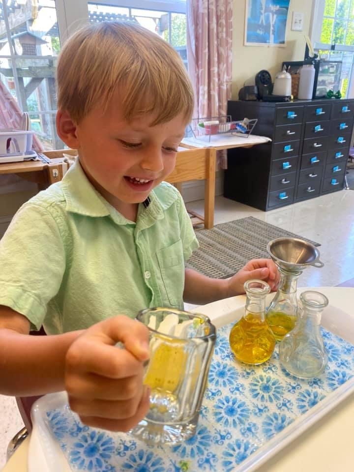 Child holding a glass over a tray with beakers and a funnel
