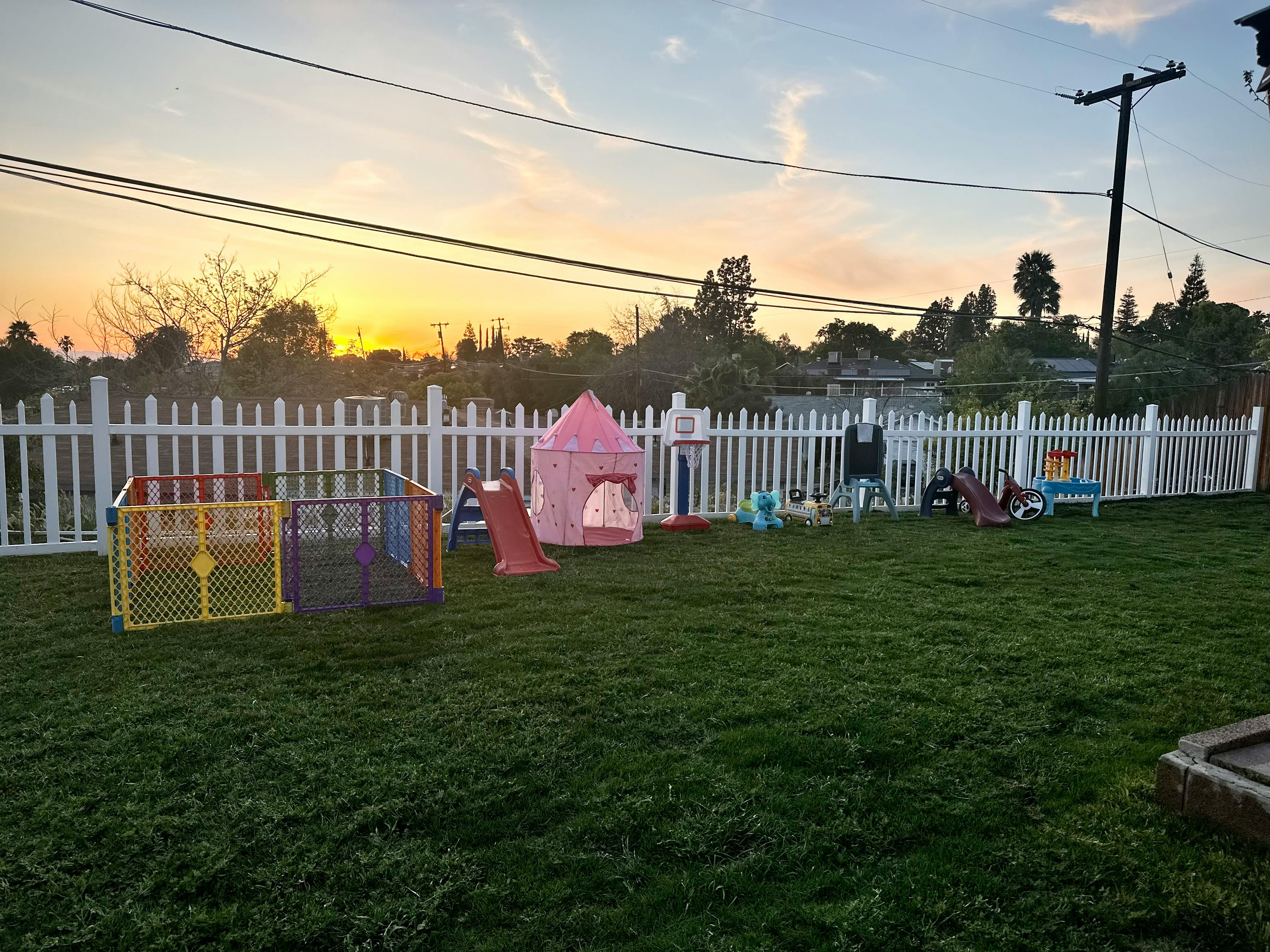 Play area with fence, playpen, tent, and slide in a grassy yard