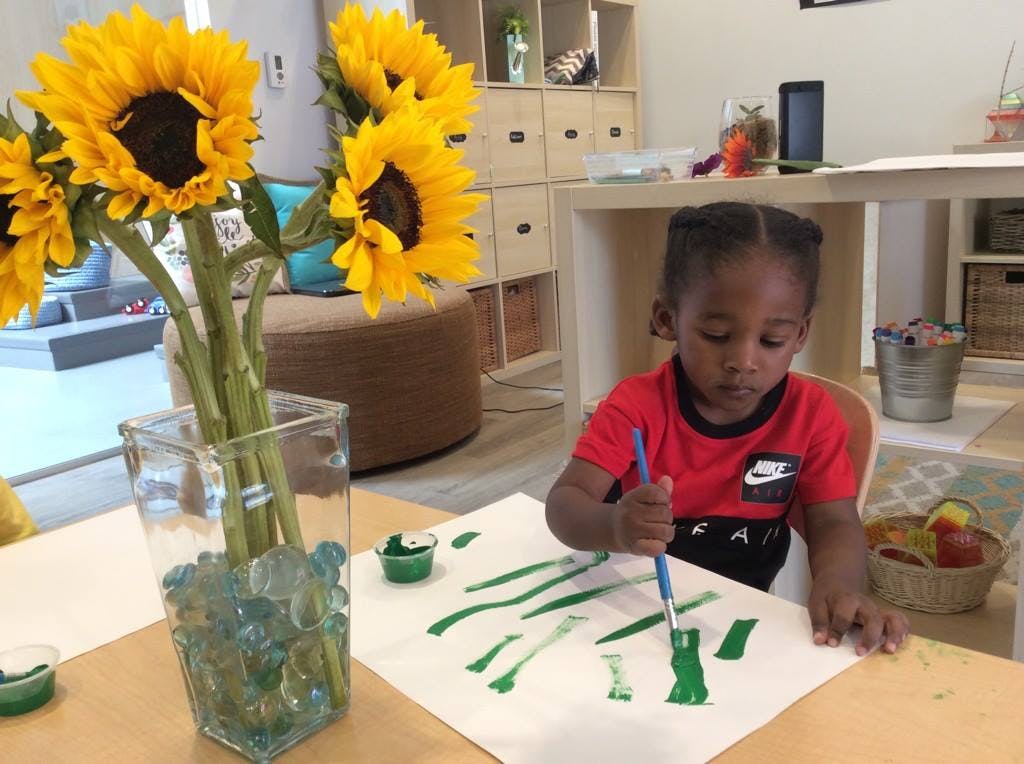 Child painting with green paint and a paintbrush