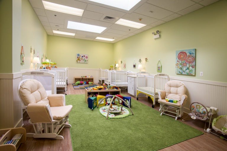 Nursery room with multiple cribs, rocking chairs, and play mats