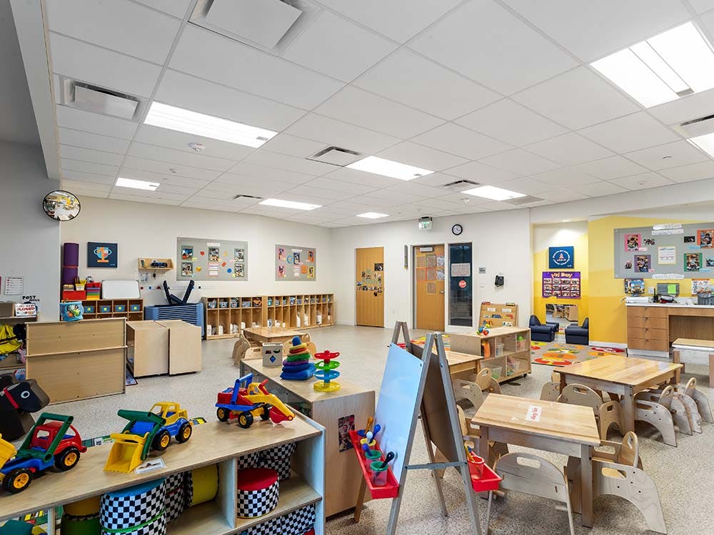 Classroom with child-sized tables and chairs, shelves with toys, and wall decorations