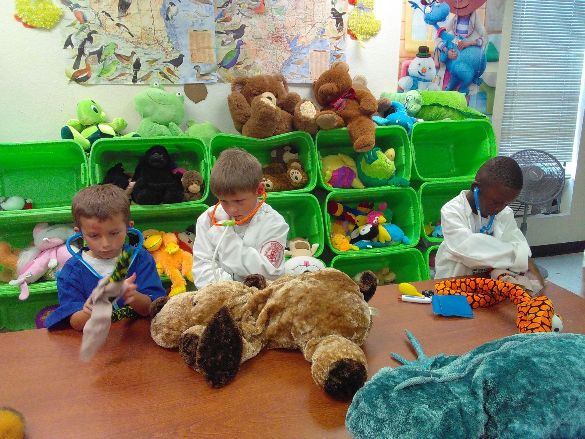 Three children playing with stuffed animals in a room with green bins of toys