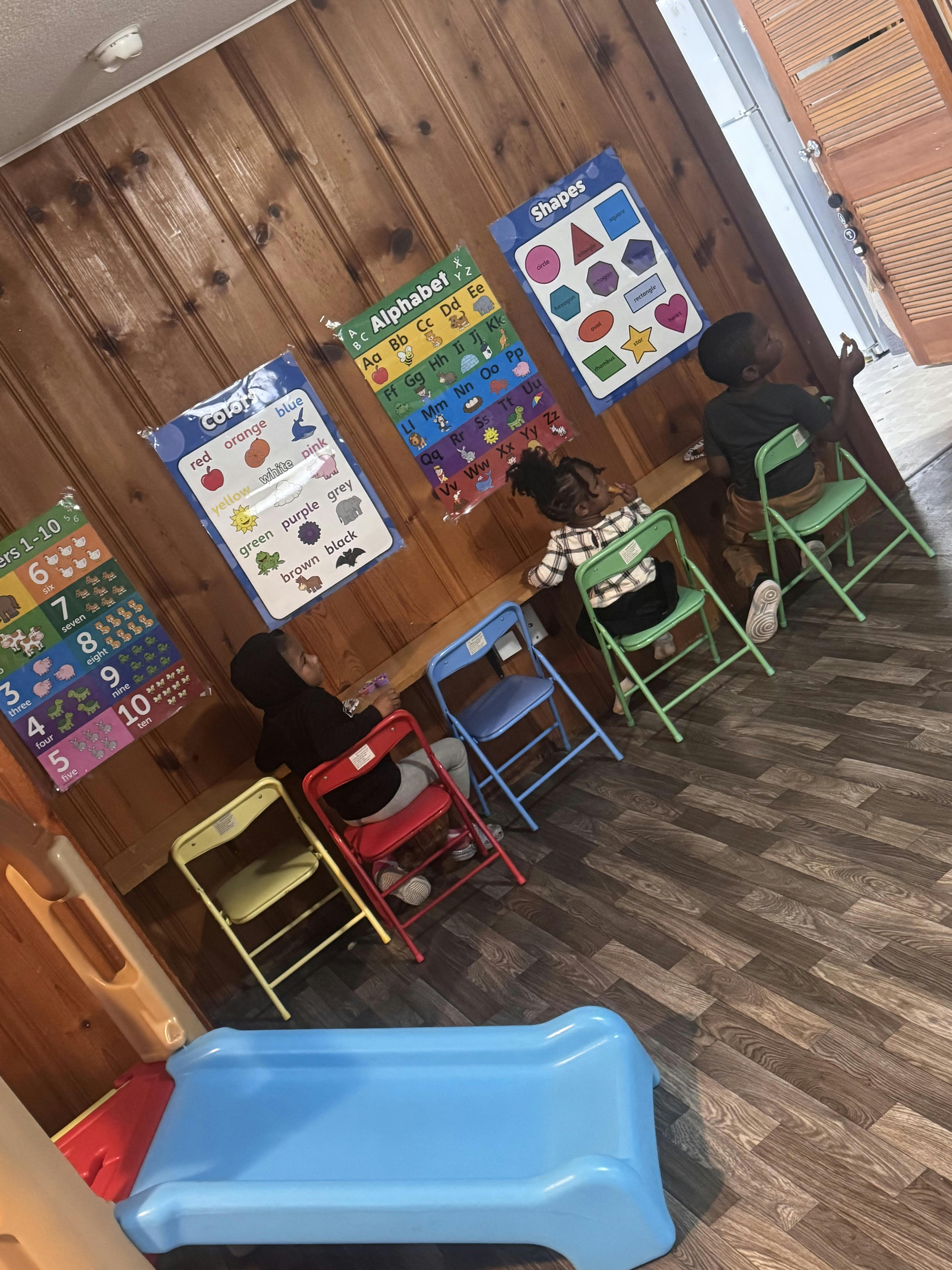 Children sitting at small tables in a classroom with educational posters