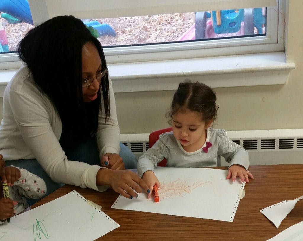Person helping a child draw with a crayon at a table