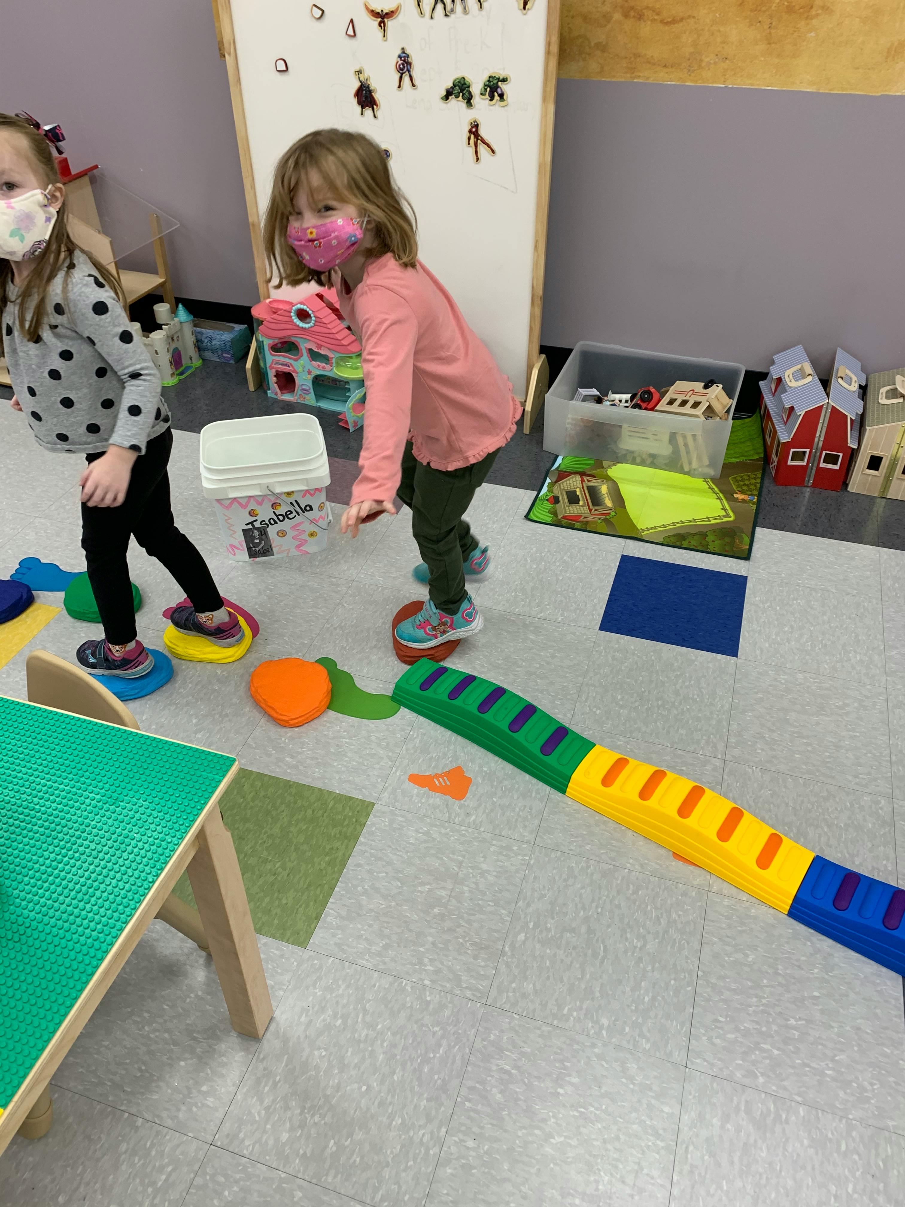 Two children wearing masks playing with balance toys