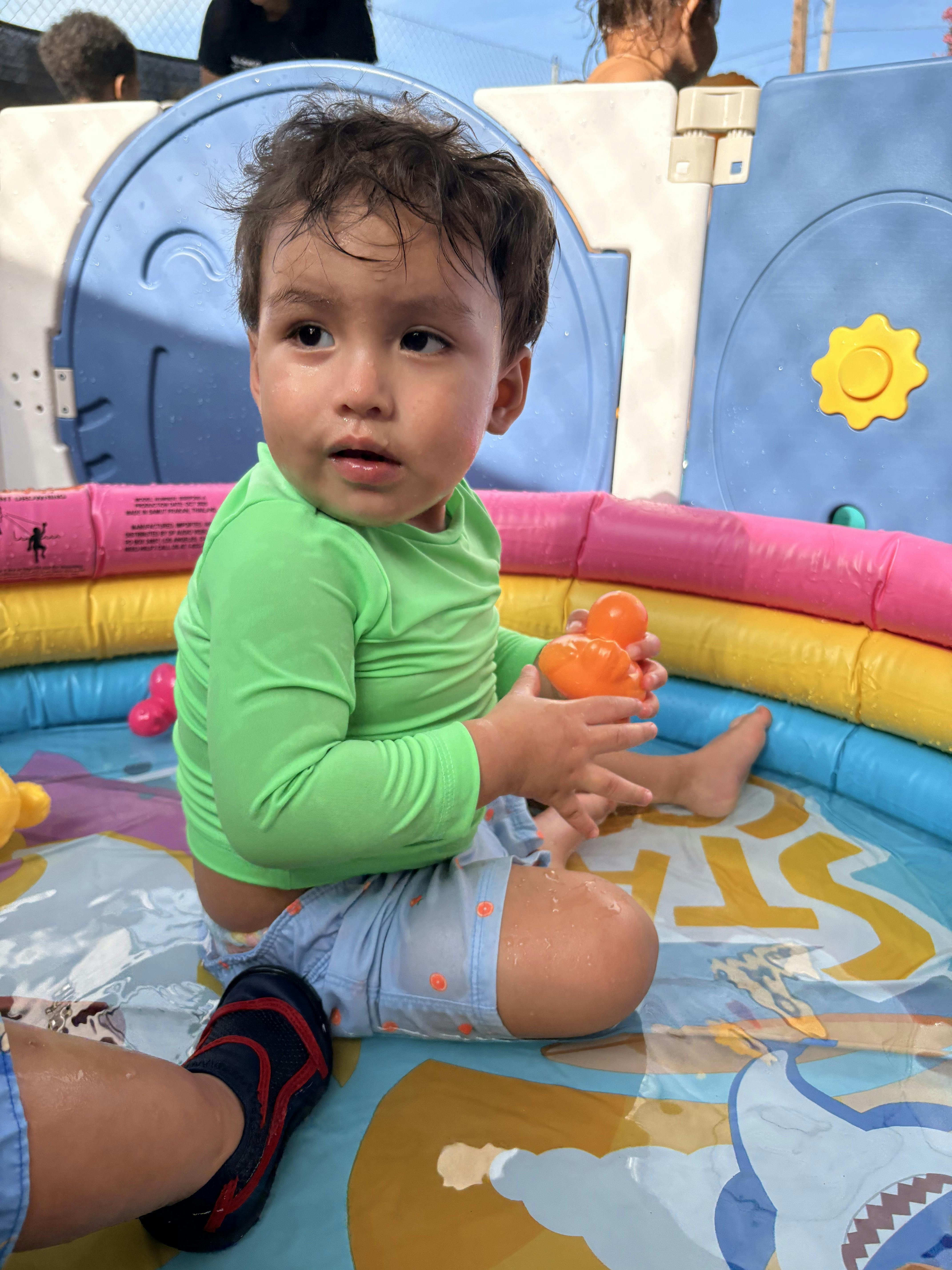 Child sitting in a plastic wading pool holding an orange toy