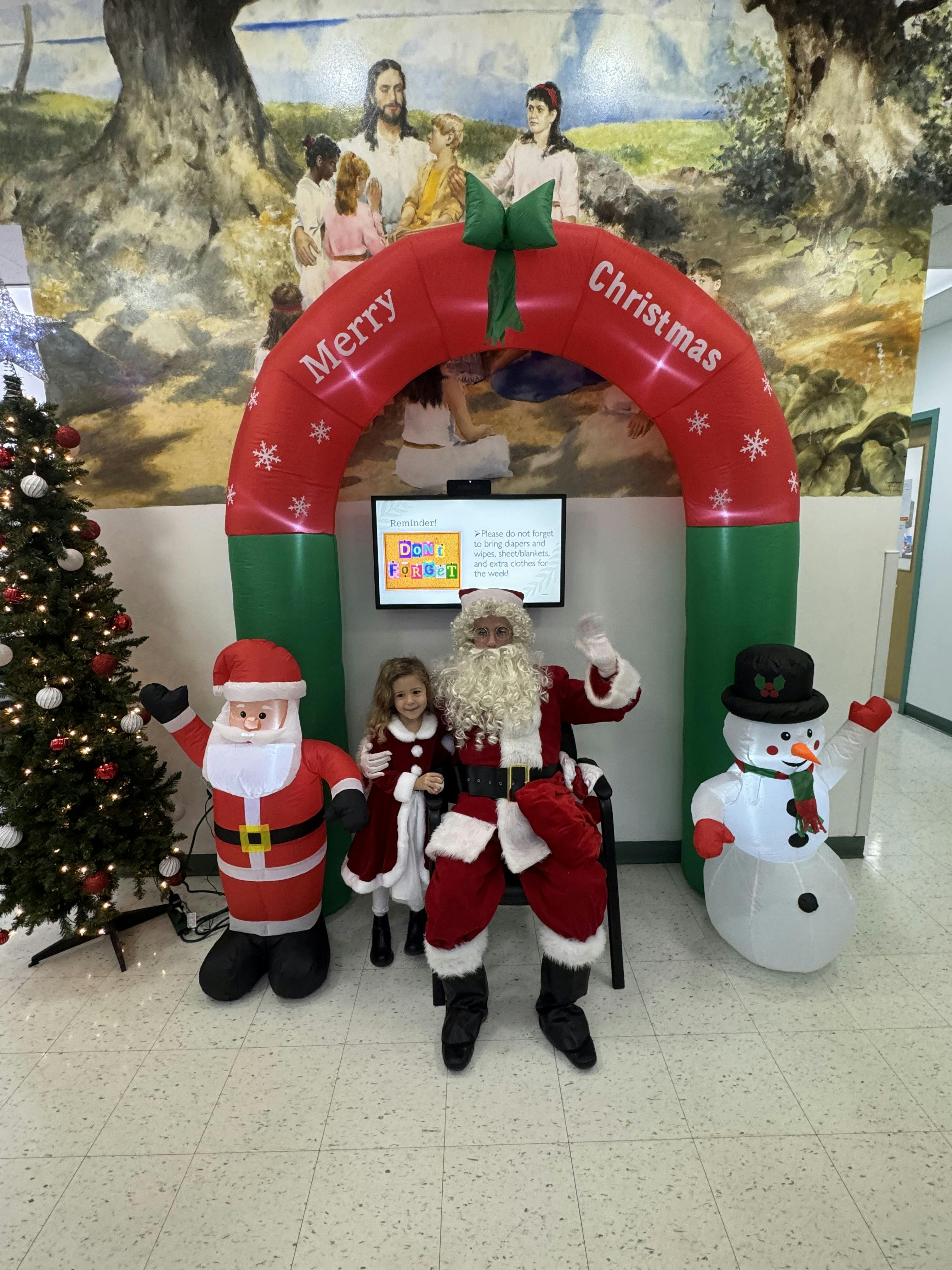 Santa Claus sitting with a child next to an inflatable Christmas arch