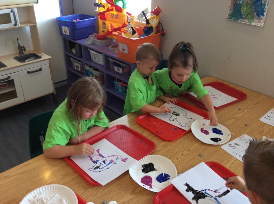 Children painting at a table in a classroom