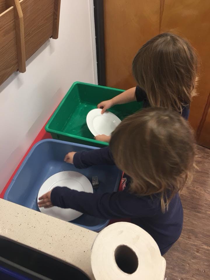 Two children washing dishes in plastic bins