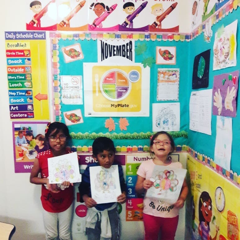 Three children holding up drawings in a classroom