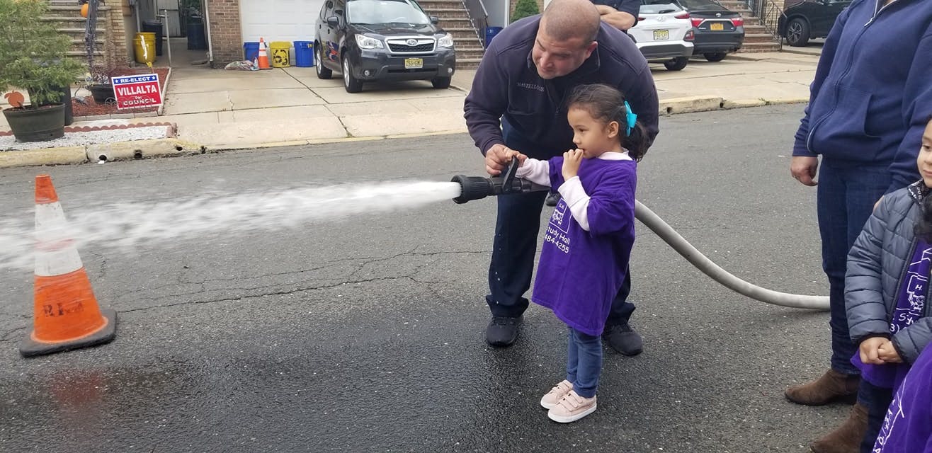 Adult helping a child spray water from a hose