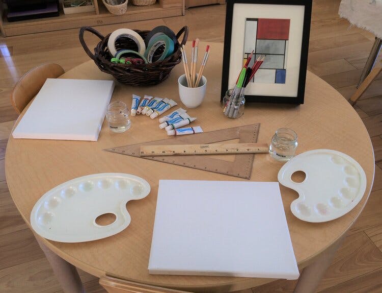 Art supplies on a round wooden table, including canvases, palettes, and paints