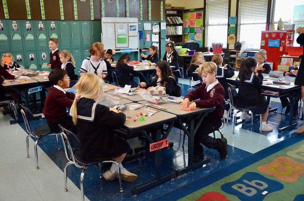 Children in school uniforms working on crafts at desks in a classroom