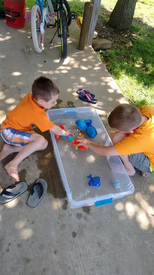Two children playing with toys in a container of water
