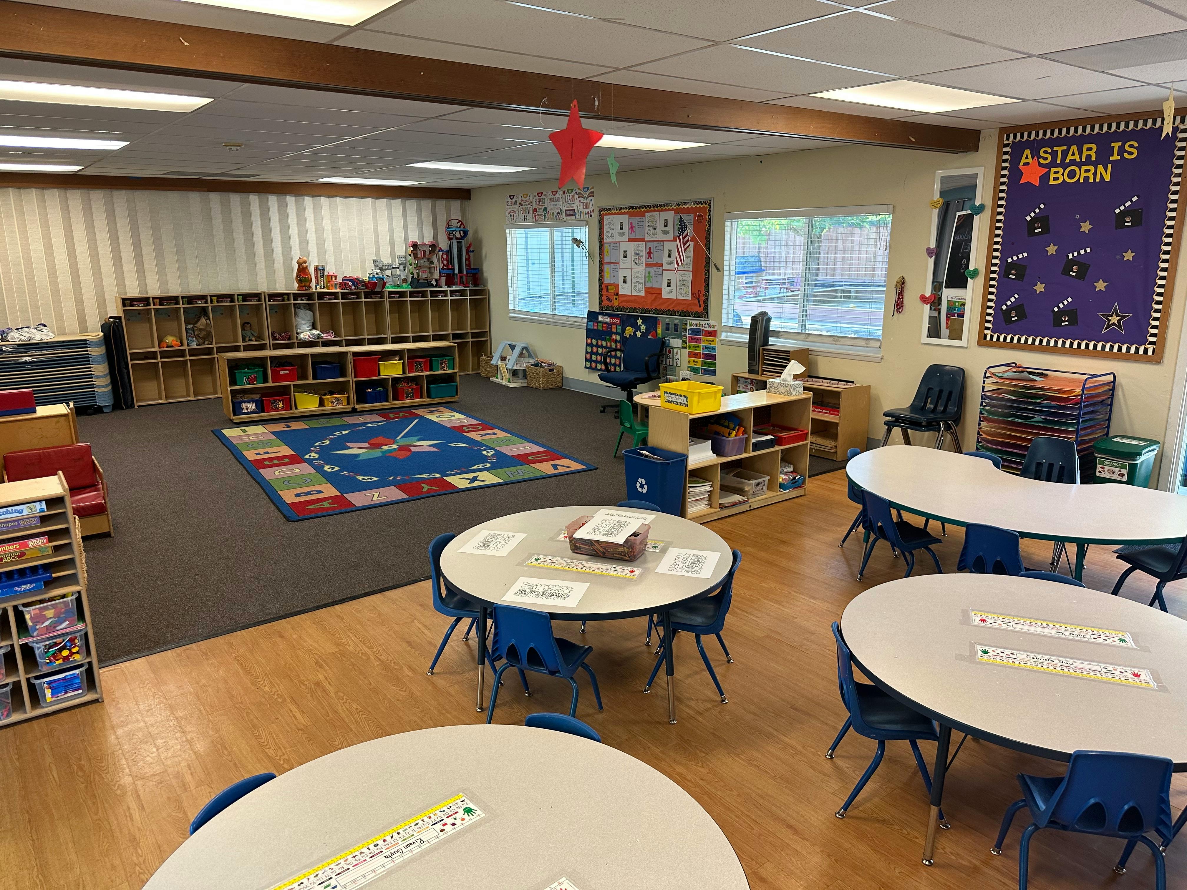 Classroom with small tables and chairs, a rug, and shelves