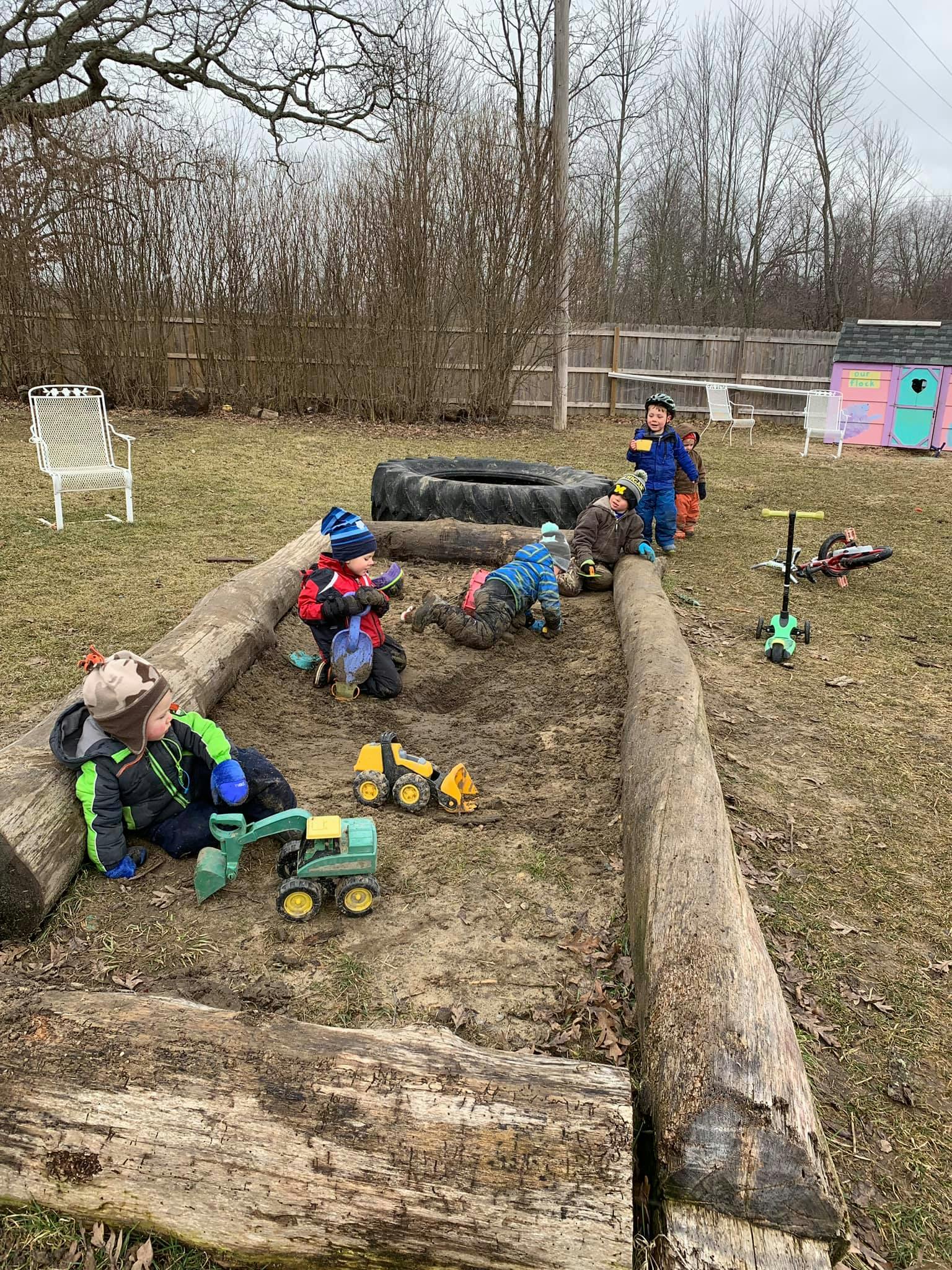 Children playing with toy trucks in a dirt area with logs