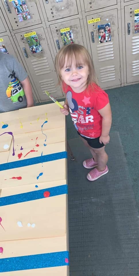 Child holding a paintbrush next to a paint-splattered surface