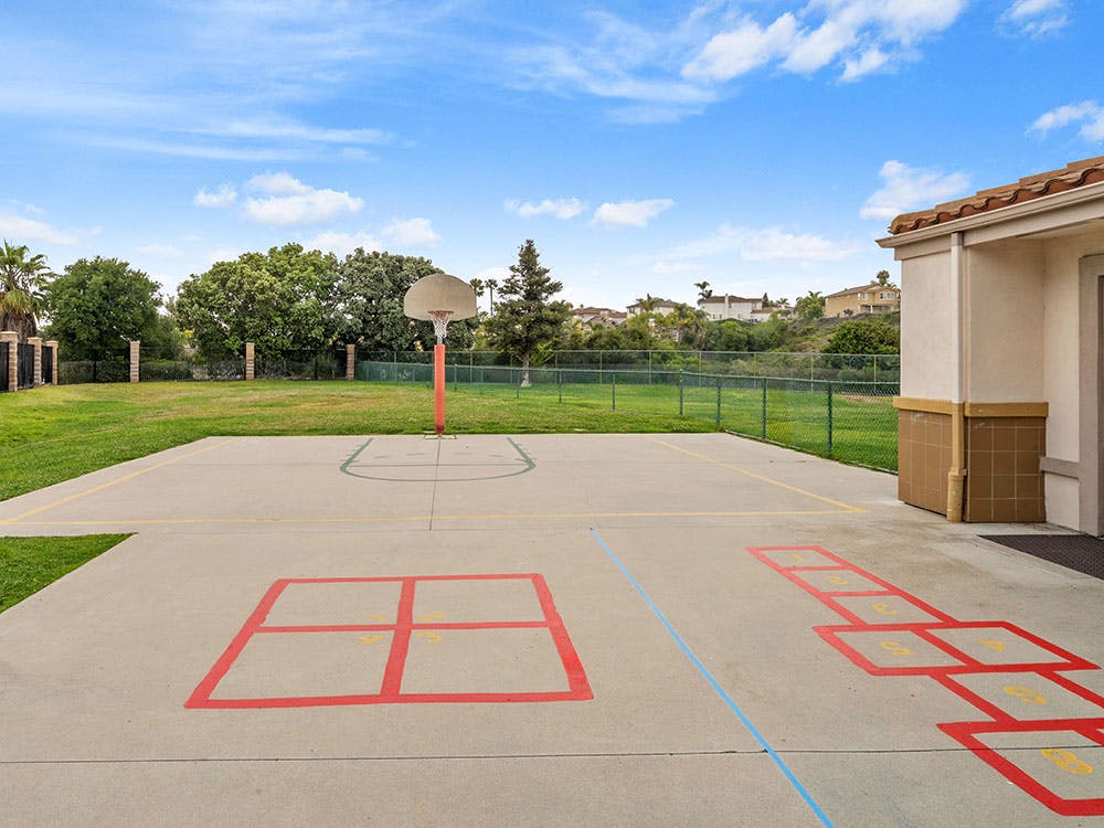 Basketball hoop on a paved court with hopscotch and four square outlines