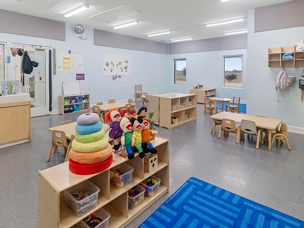 Classroom with small tables, chairs, and shelves holding toys