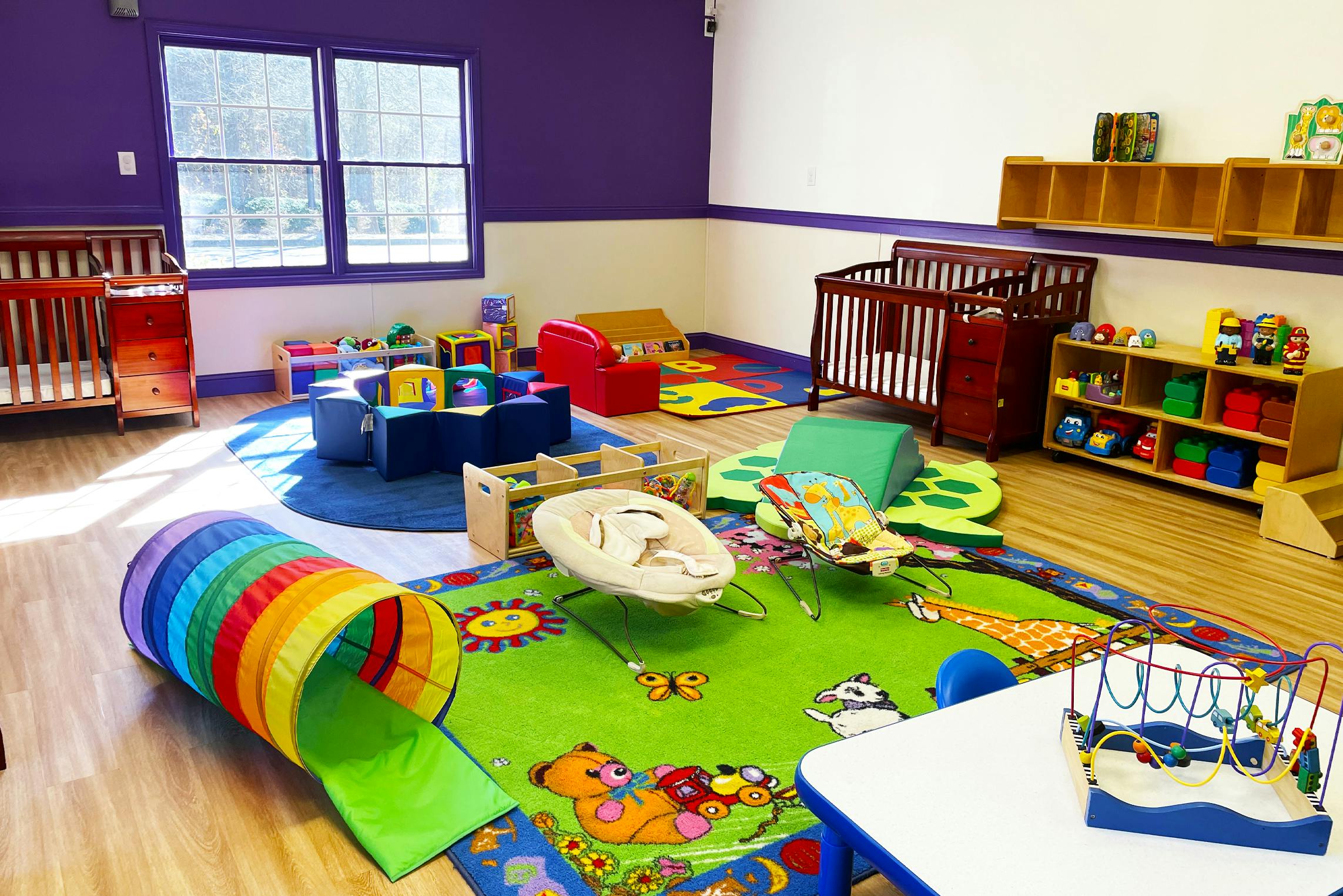 Baby room with cribs, play tunnel, bouncers, and colorful rugs and toys