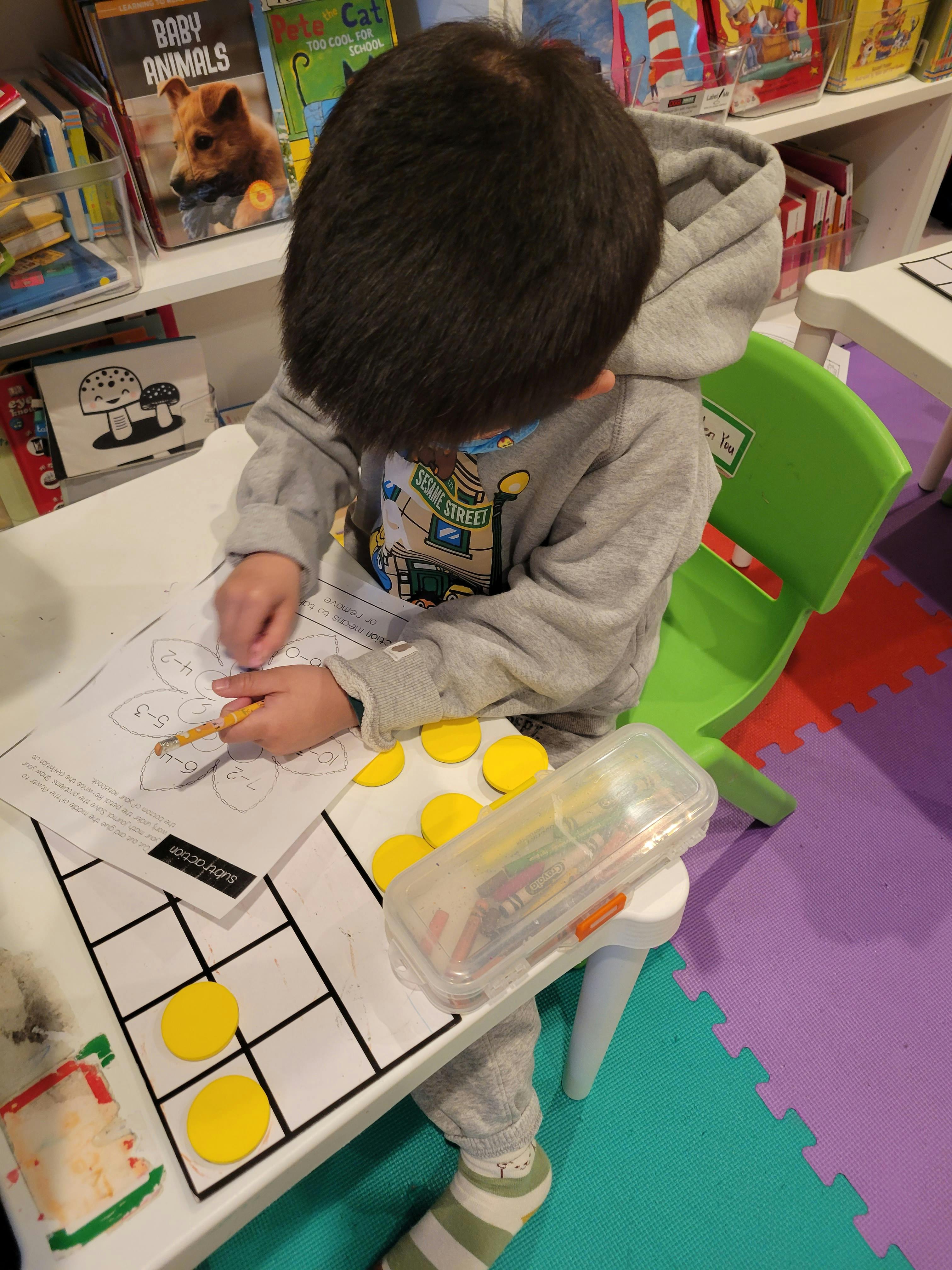 Child writing on a subtraction worksheet with a pencil