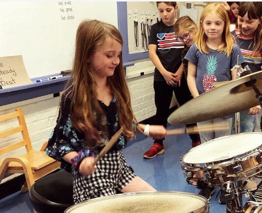 Child playing drums with other children watching
