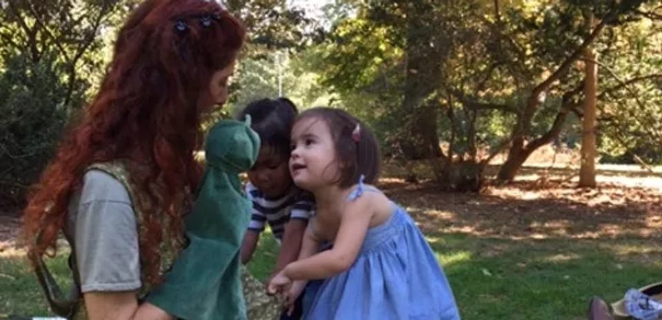 Person with puppet interacting with two children outdoors