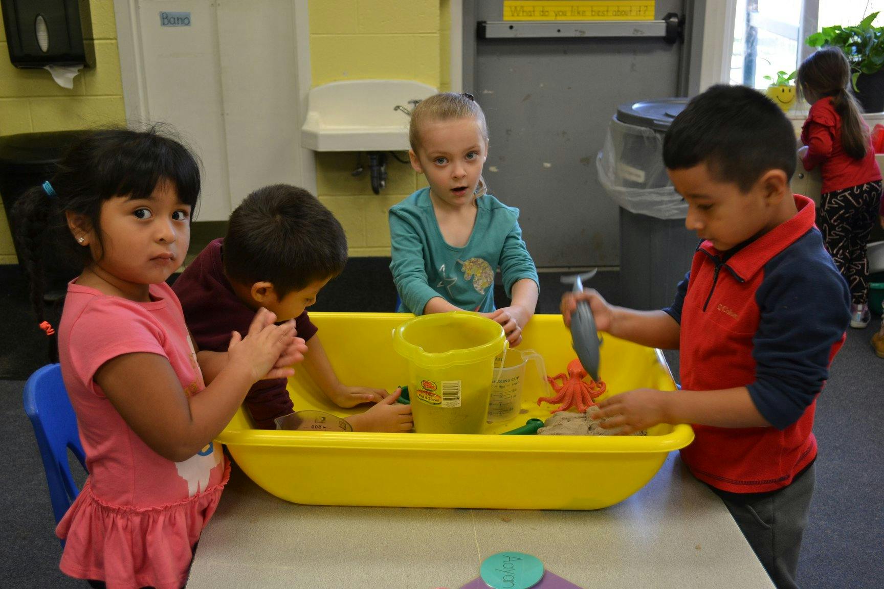 Children playing with sand and toys in a yellow bin