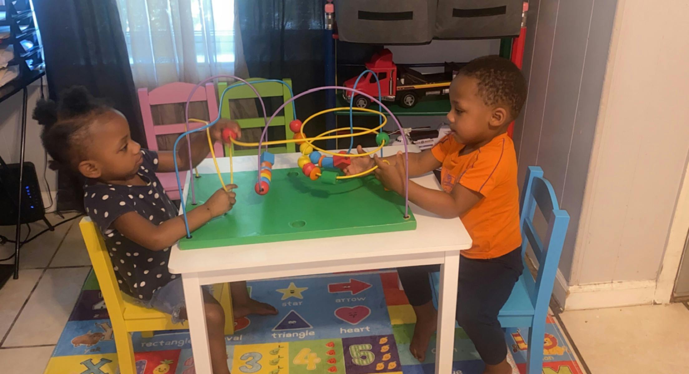 Two children playing with a bead maze on a small table