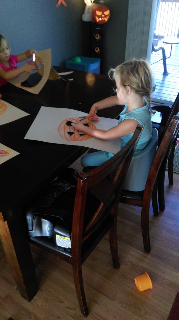 Child cutting out a drawing of a pumpkin at a table