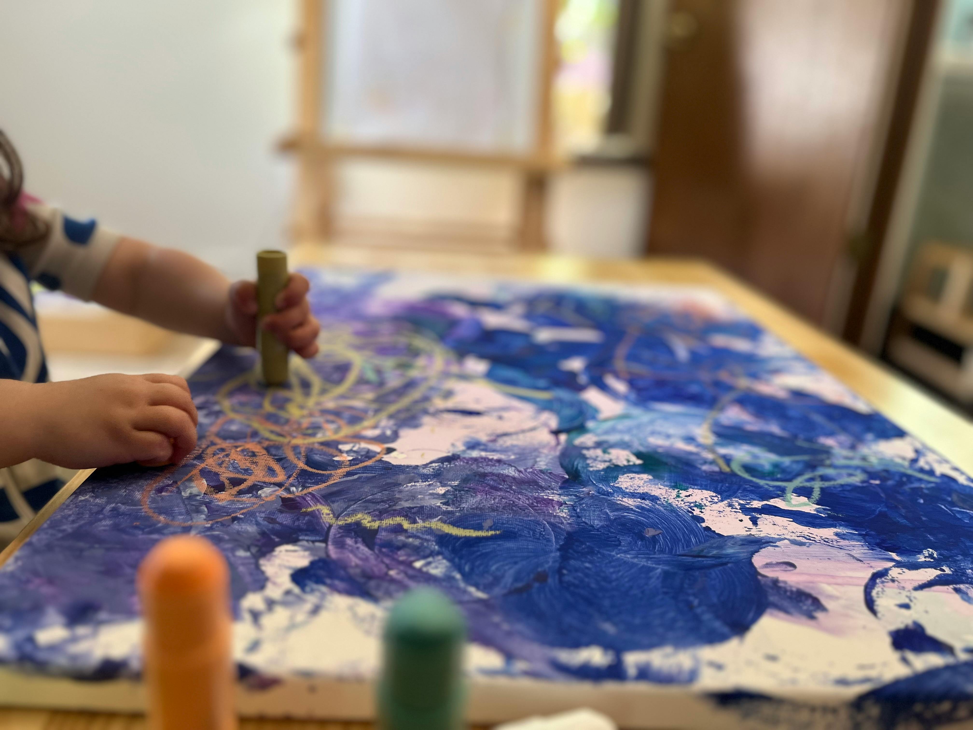 Child's hands drawing on a canvas with a crayon