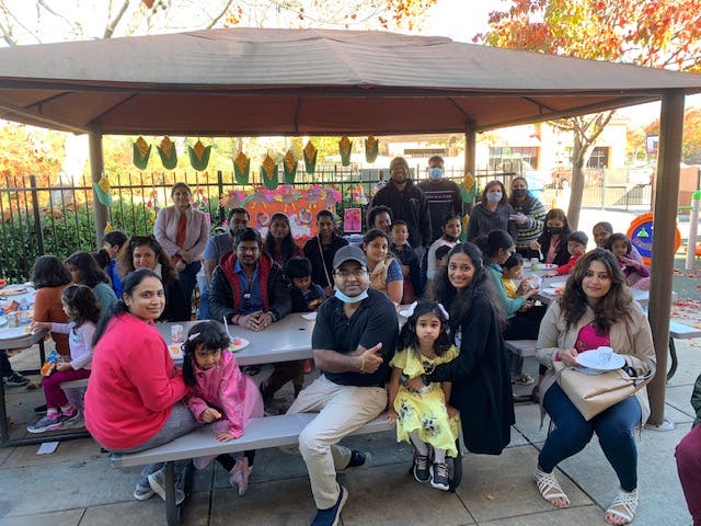 Group of people and children sitting at picnic tables under a canopy