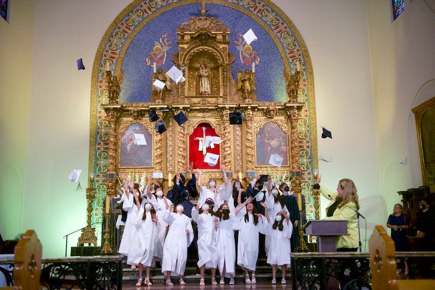 Students in white robes throwing graduation caps in the air during a ceremony