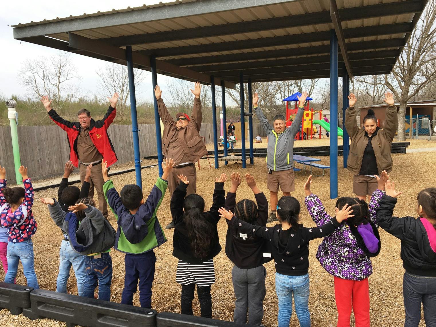 Adults and children with arms raised outdoors