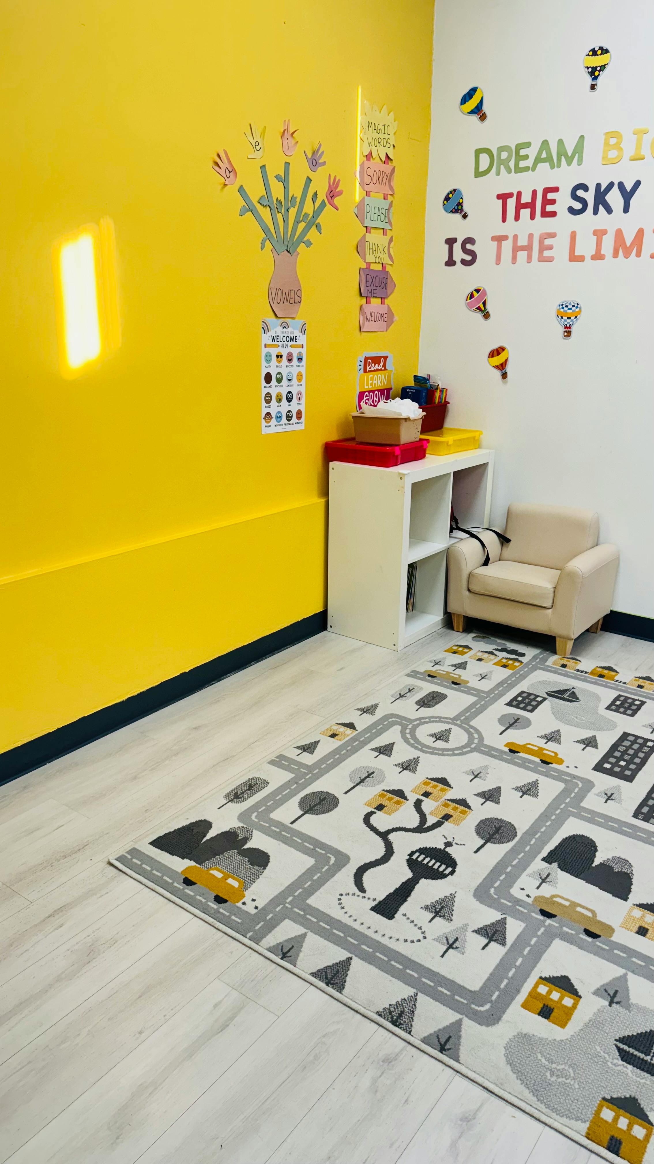 Children's play area with a yellow wall, rug with roads, and small armchair