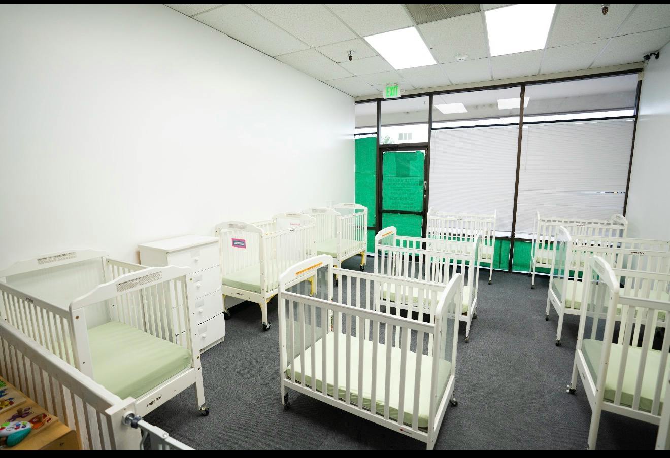 Multiple empty cribs arranged in a childcare room
