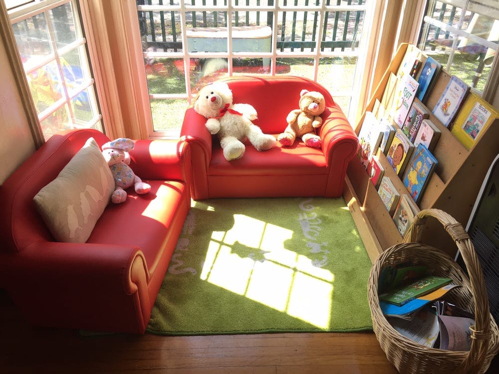 Two red child-sized sofas with stuffed animals and a book display