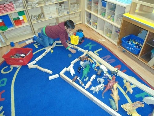 Child playing with blocks and animal toys on a blue rug