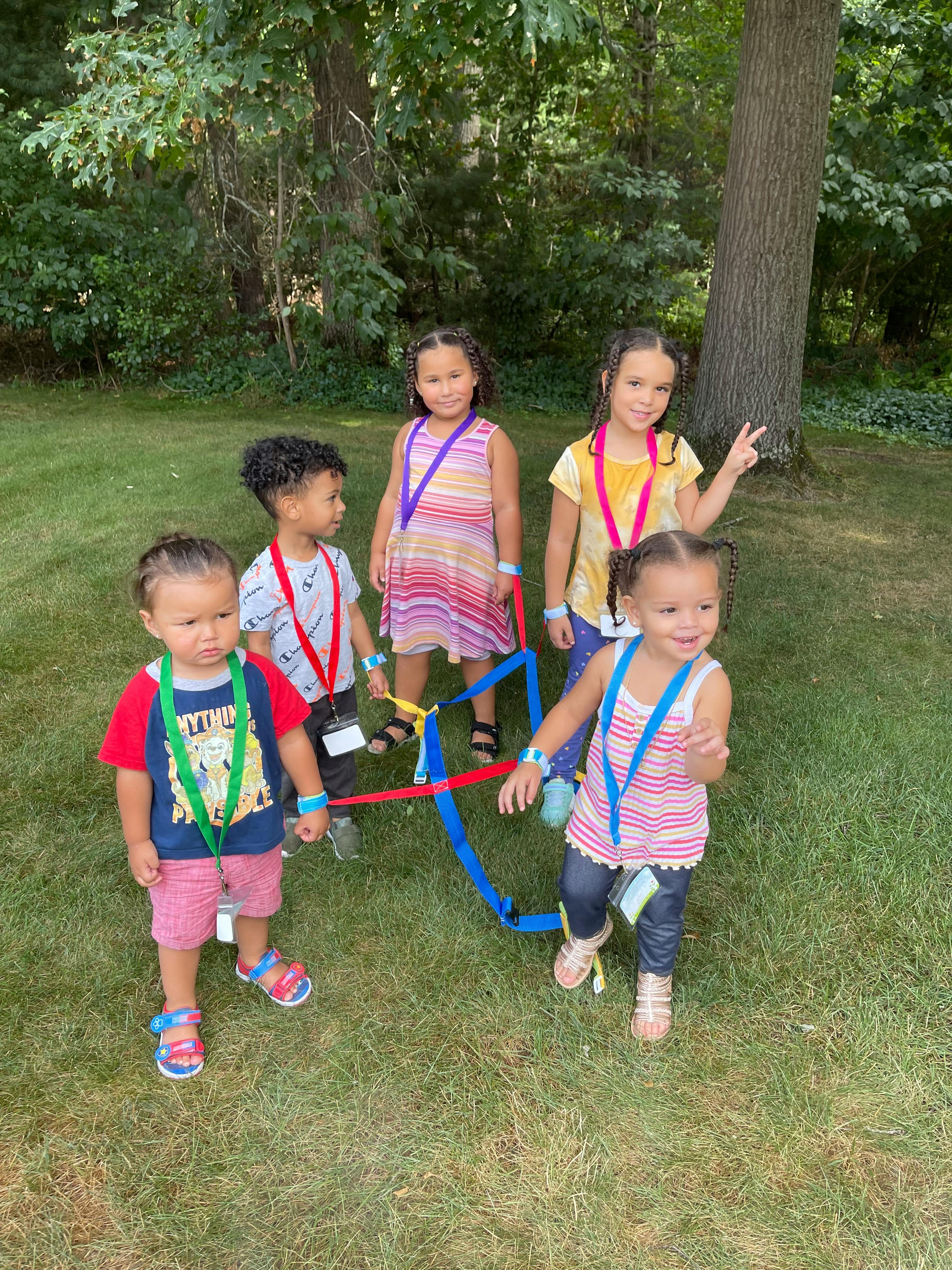 Five children standing in grass with colorful straps connecting straps
