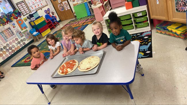 Children at a table with two pizzas on a baking sheet