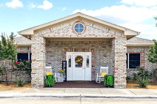 Front entrance of a brick building with a white door and two rocking chairs